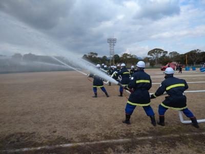 空に向かって一斉に水を噴射し放水点検を受けている消防団員の画像