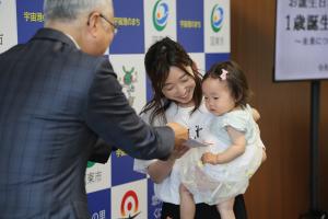 市長が１歳になった子とその保護者の方に、お祝いを渡しています