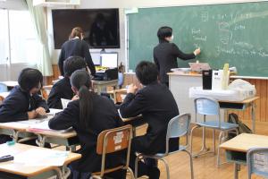 講師が黒板の前に立ち教えているところを生徒４人が聞いている