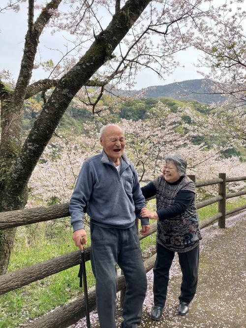 満開の桜の下で笑顔のおじいさんおばあさんの写真