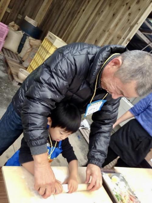 孫のピザ作りを手伝うおじいさんの写真